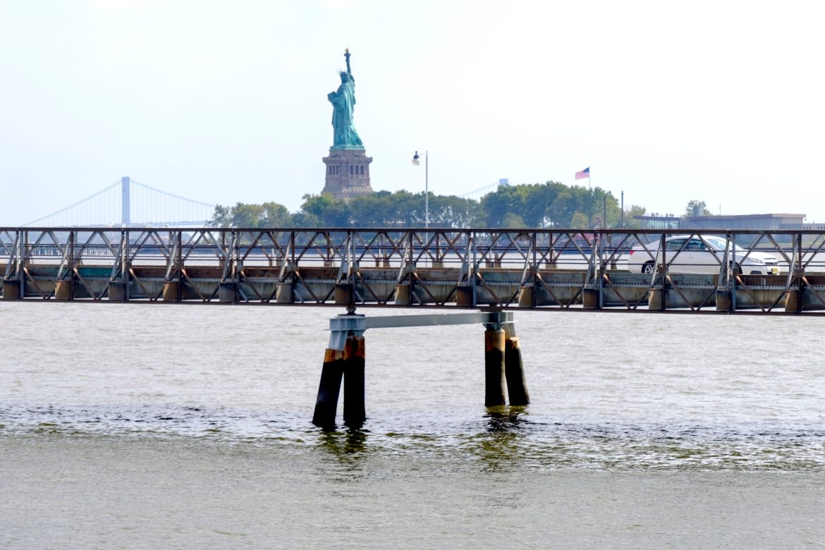 Um carro atravessa a ponte de Ellis Island a Jersey City, com a Estátua da Liberdade e a Ponte Verrazzano-Narrows ao fundo em 30 de agosto de 2019.