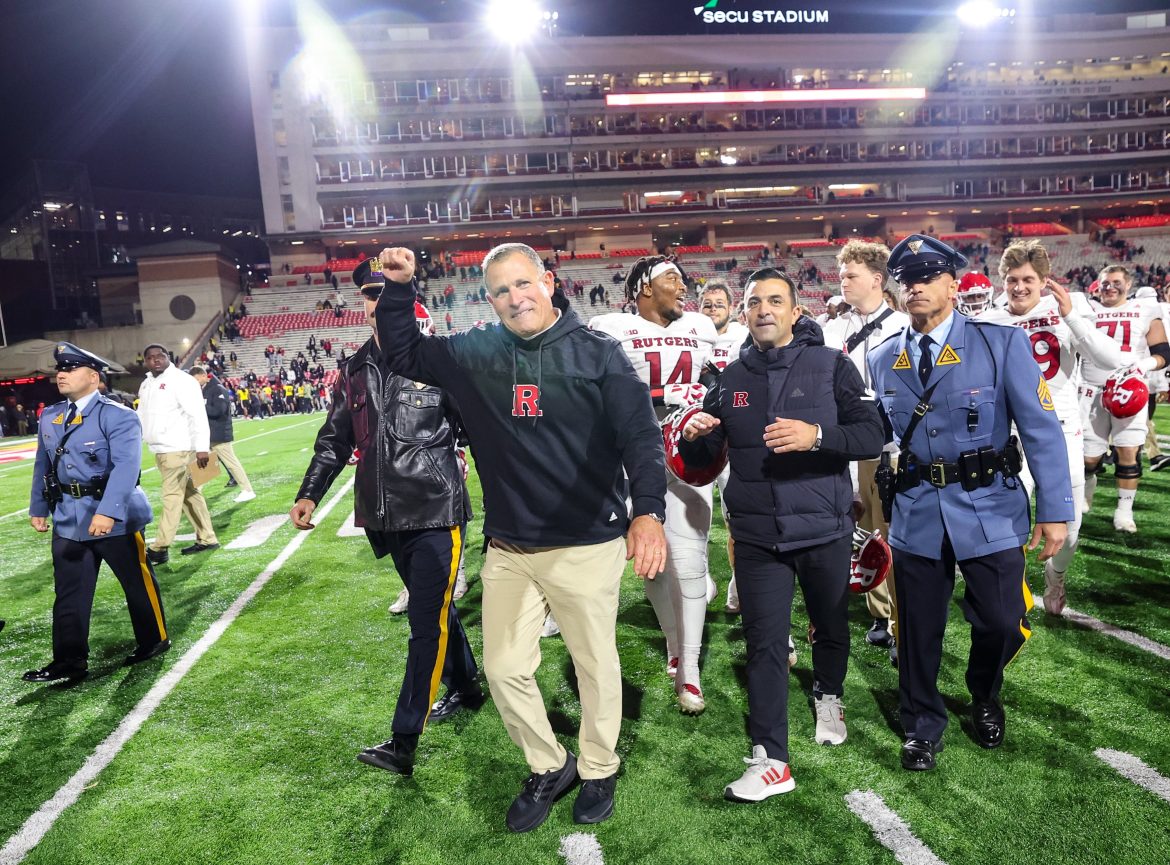 Ladeado pelo diretor atlético interino da Rutgers, Ryan Pisarri, o técnico Greg Schiano levanta o punho enquanto sai do campo depois que os Scarlet Knights derrotaram Maryland, no sábado, 16 de novembro de 2024, para se tornarem elegíveis para o bowl.